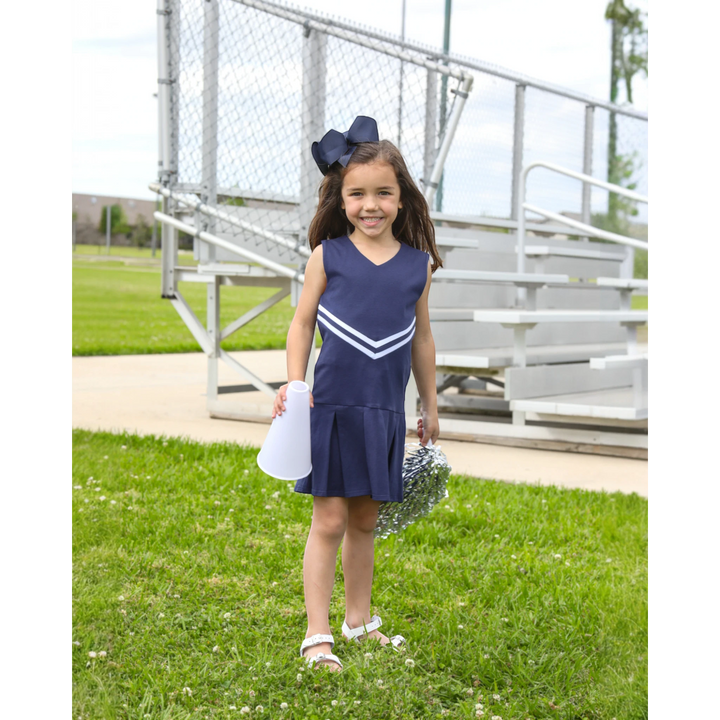 Young girl wearing a That Store navy cheer uniform dress with white stripes, holding a megaphone and silver pom-poms.
