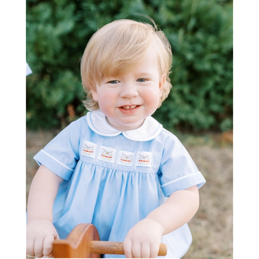 That Store Noah ribbon bubble in river royal mini gingham with drum embroidery worn by a smiling toddler boy
