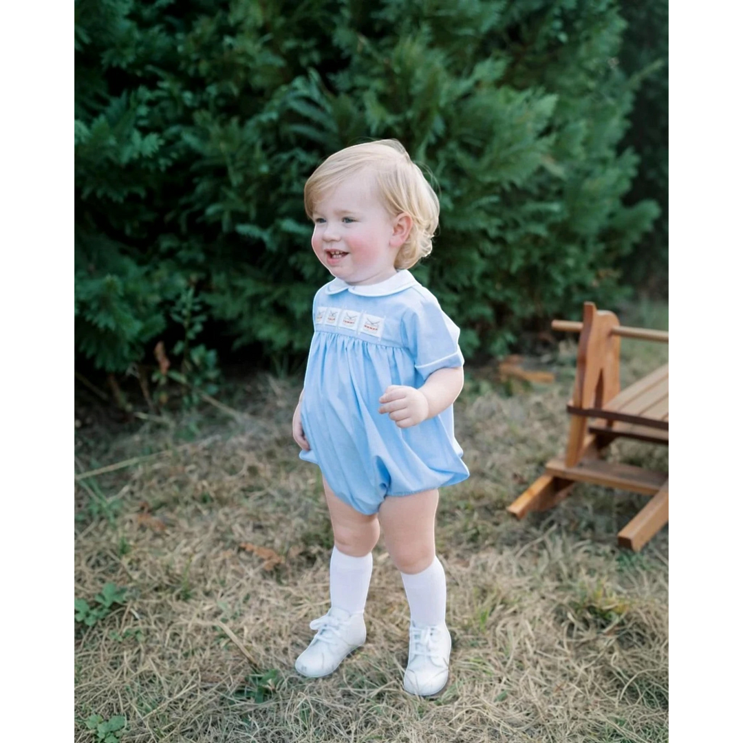 That Store Noah ribbon bubble in river royal mini gingham worn by a toddler with white socks and shoes outdoors