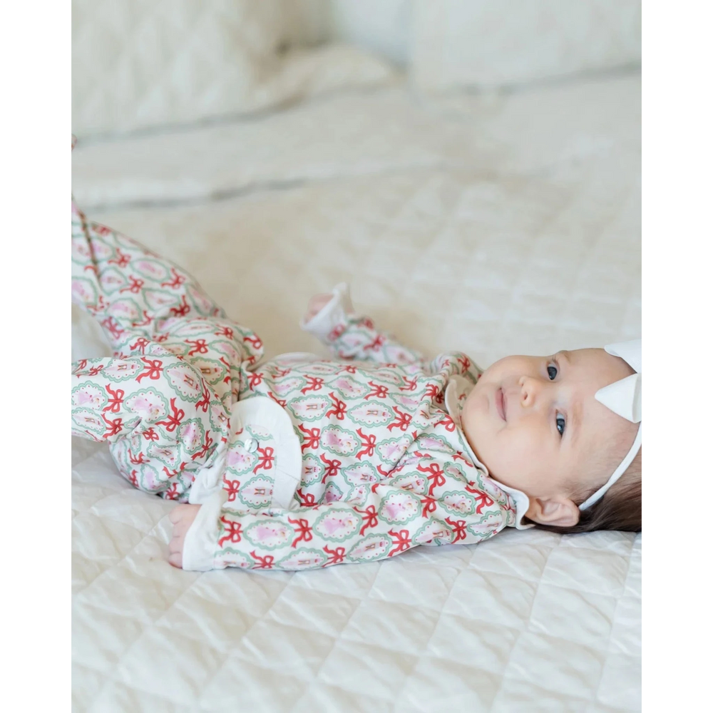 Baby girl wearing a That Store long-sleeved pima cotton footed onesie with a red and green Nutcracker ballet print.