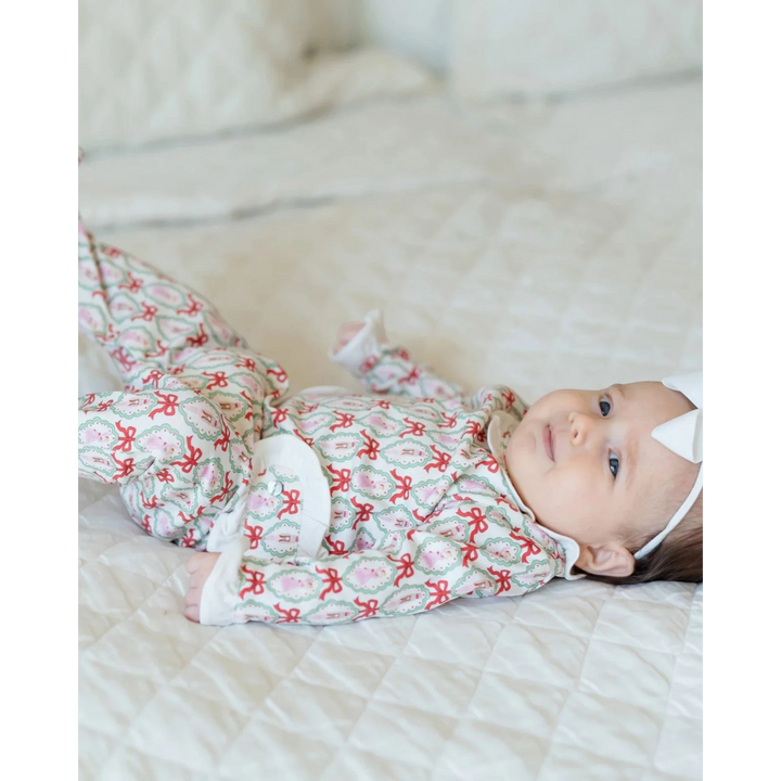 Baby girl wearing a That Store long-sleeved pima cotton footed onesie with a red and green Nutcracker ballet print.