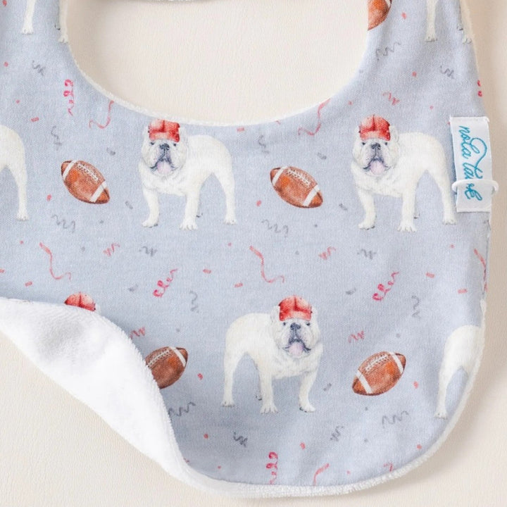 That Store organic cotton baby bib featuring a light blue pattern of bulldogs in red hats and footballs.