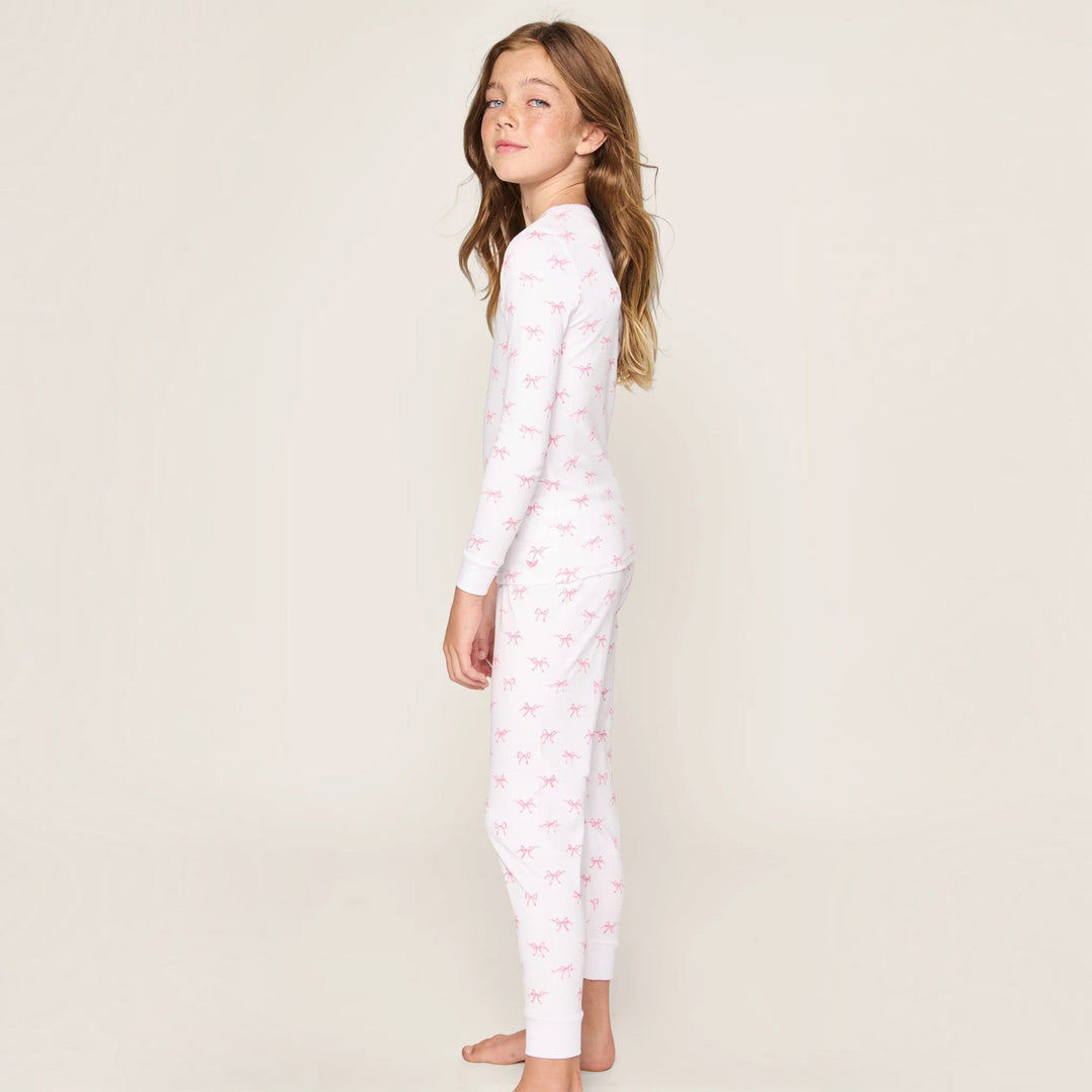 A young girl wearing a That Store long-sleeve Pima cotton pajama set in white with a pink Blushing Bows print.