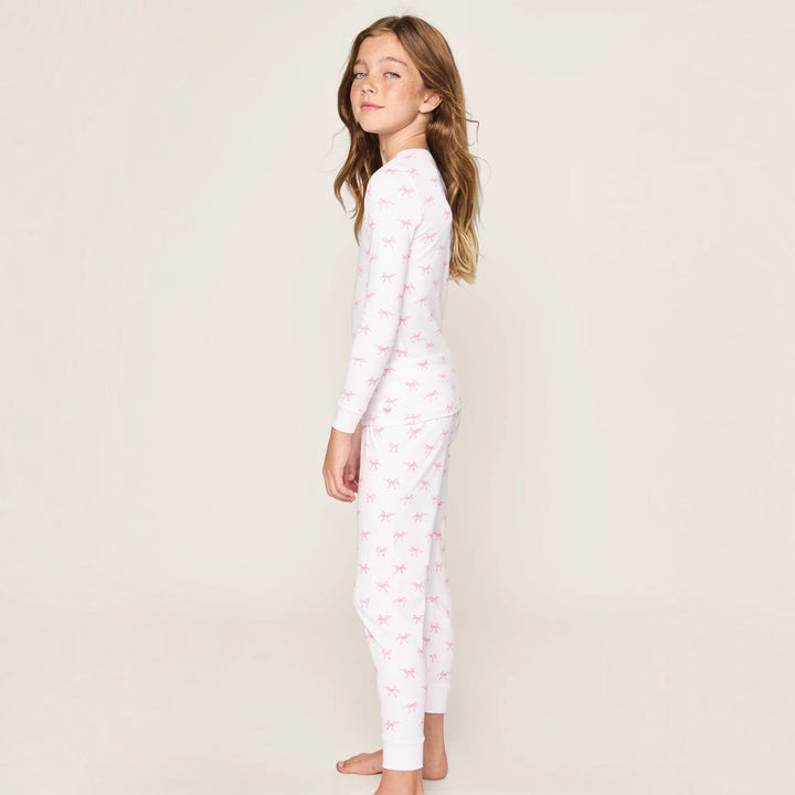 A young girl wearing a That Store long-sleeve Pima cotton pajama set in white with a pink Blushing Bows print.