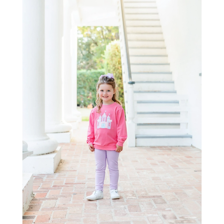 Young girl wearing a That Store pink French terry pullover with a white castle graphic, paired with lavender leggings.