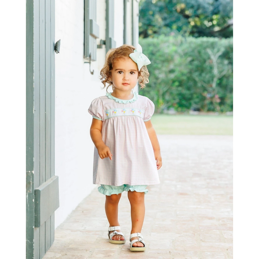Toddler girl wearing a That Store pink checkered bloomer set with balloon embroidery, mint ribbon, and white sandals.