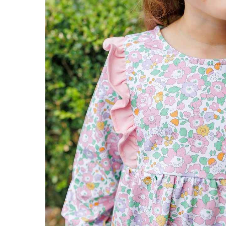 That Store pink floral bubble romper with ruffled shoulder details on a young girl in a garden setting