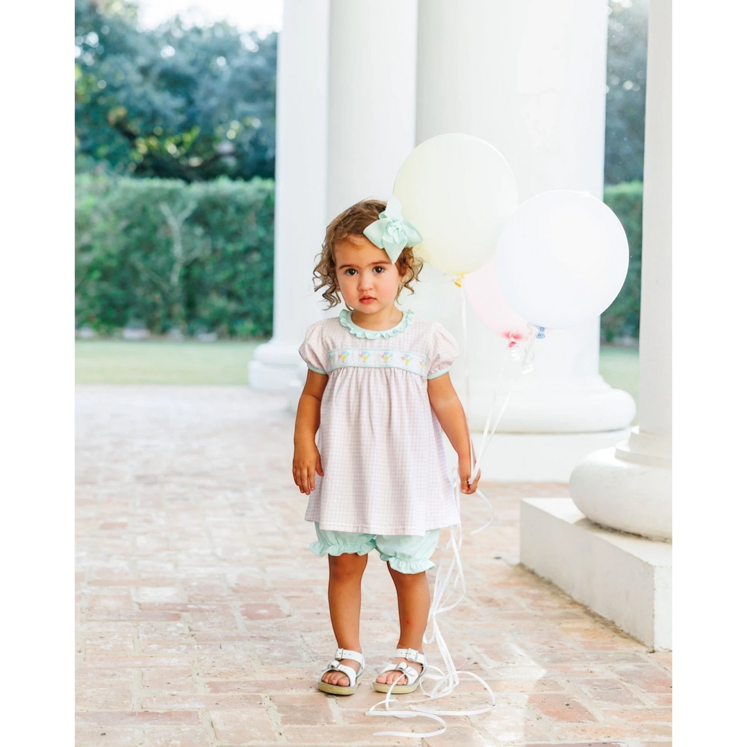 Toddler girl wearing a That Store pink gingham bloomer set with balloon embroidery, ribbon accents, and a hair bow.