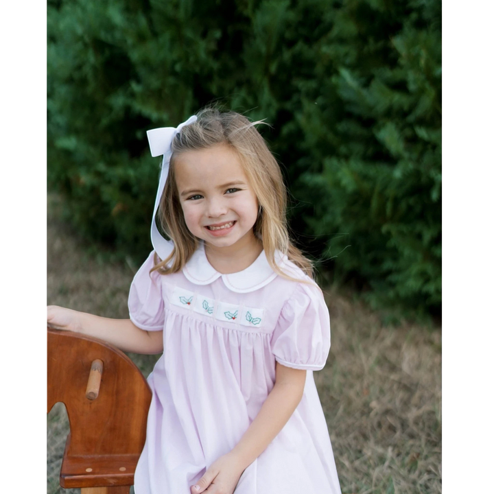 Young girl wearing a That Store pink mini gingham dress with a white collar and interchangeable holiday ribbon detail