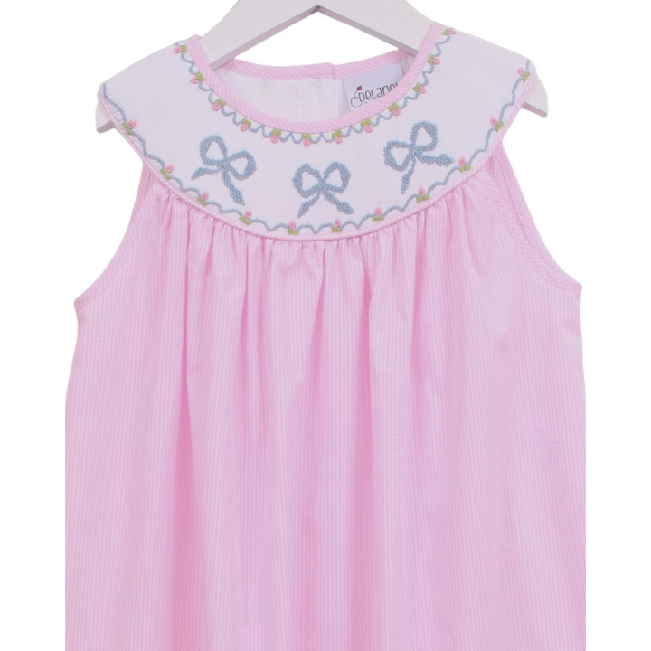That Store pink gingham sleeveless dress with a white smocked yoke featuring embroidered blue bows and floral detail.