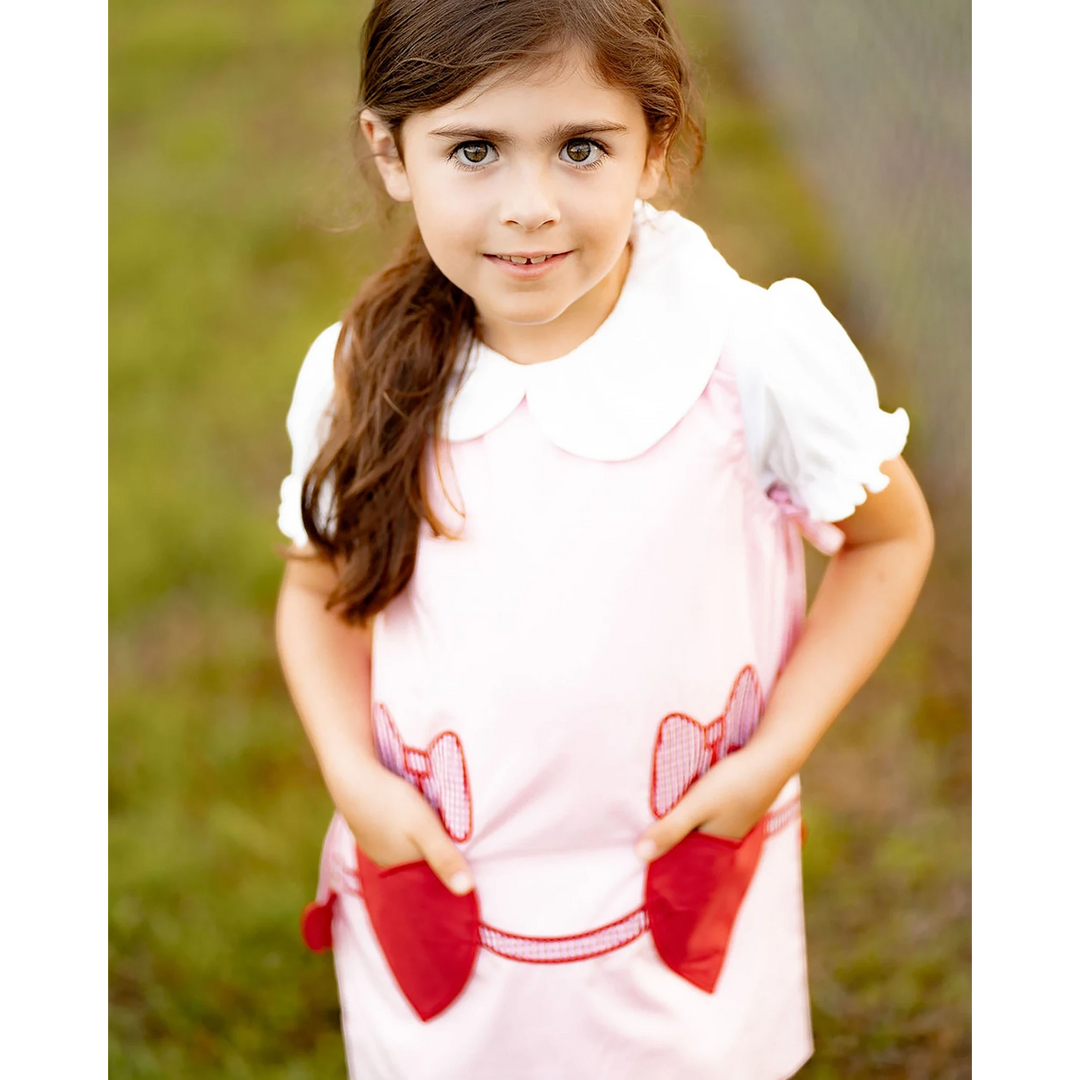 Young girl wearing a That Store Emma Pink jumper with white collar and red heart-shaped pockets with bows