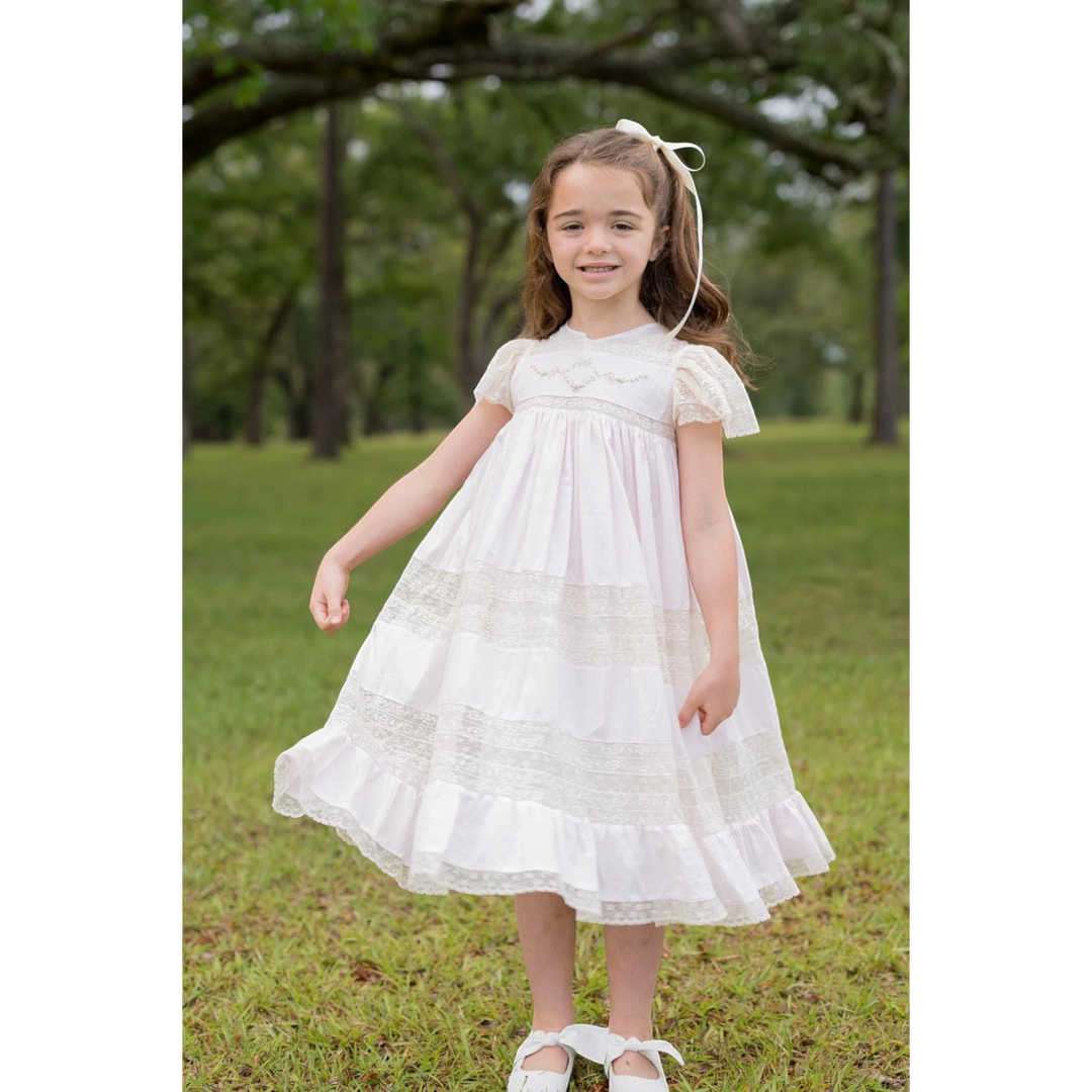 Young girl wearing a pink That Store Mary Frances cotton heirloom dress with intricate ecru lace and floral embroidery.