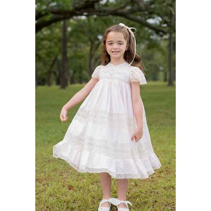 Young girl wearing a pink That Store Mary Frances cotton heirloom dress with intricate ecru lace and floral embroidery.