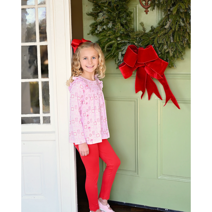 Girl wearing That Store Letters to Santa pink swing top and red knit leggings standing by a festive green door.