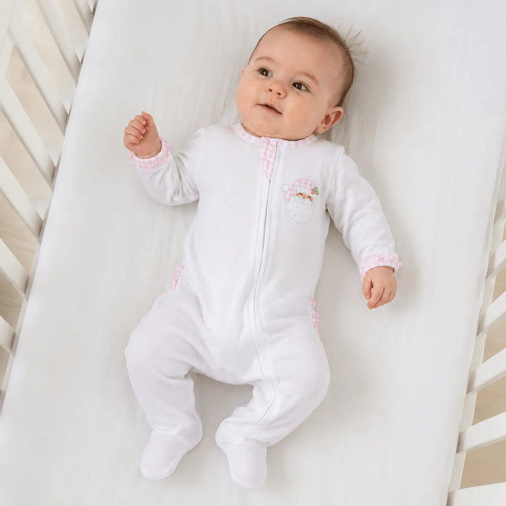 Baby wearing a That Store white Pima cotton footie with pink gingham ruffles and a Santa applique in a crib