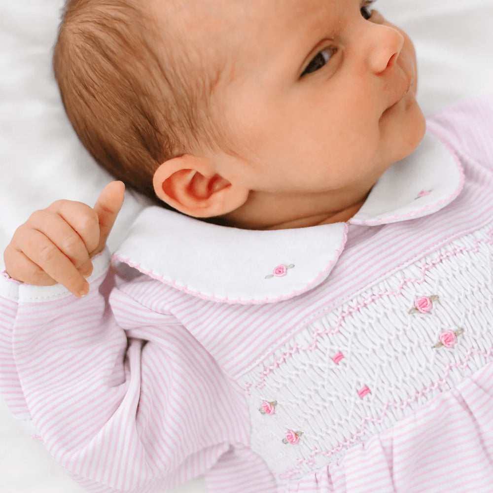 That Store baby girl wearing a pink micro-stripe footie with hand-smocked chest, rosebud embroidery, and Peter Pan collar