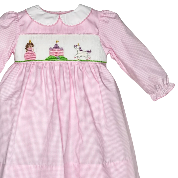 That Store pink gingham dress with hand-smocked fairytale scene, peter pan collar, and long sleeves for girls.