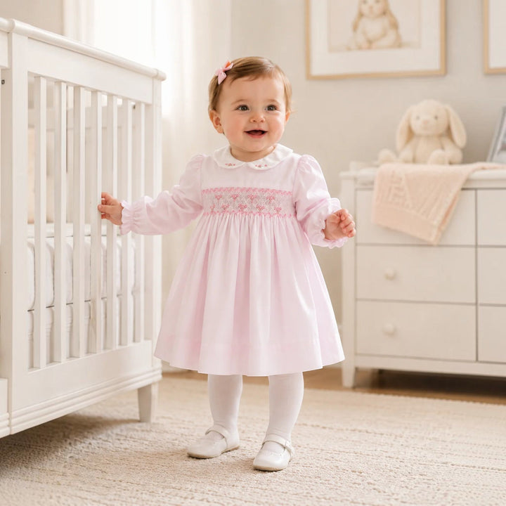 That Store pink girls dress with corded smocking, embroidered collar, and rosette details worn by a toddler.