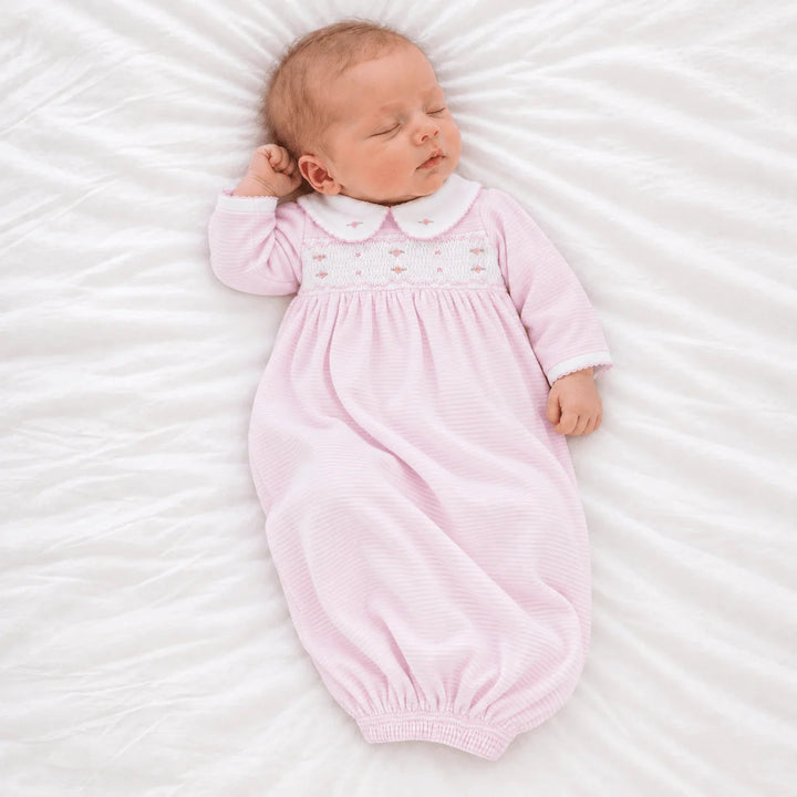 Newborn baby sleeping in a That Store pink micro-stripe smocked gown with a Peter Pan collar and rosebud embroidery.
