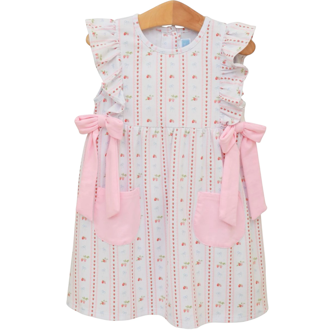 That Store pink strawberry print cotton dress with ruffled sleeves, side bows, and pockets on a wooden hanger.
