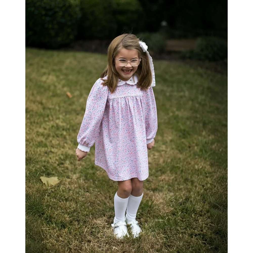 Young girl wearing a That Store long sleeve floral dress with pumpkin embroidery on the collar in a grassy field
