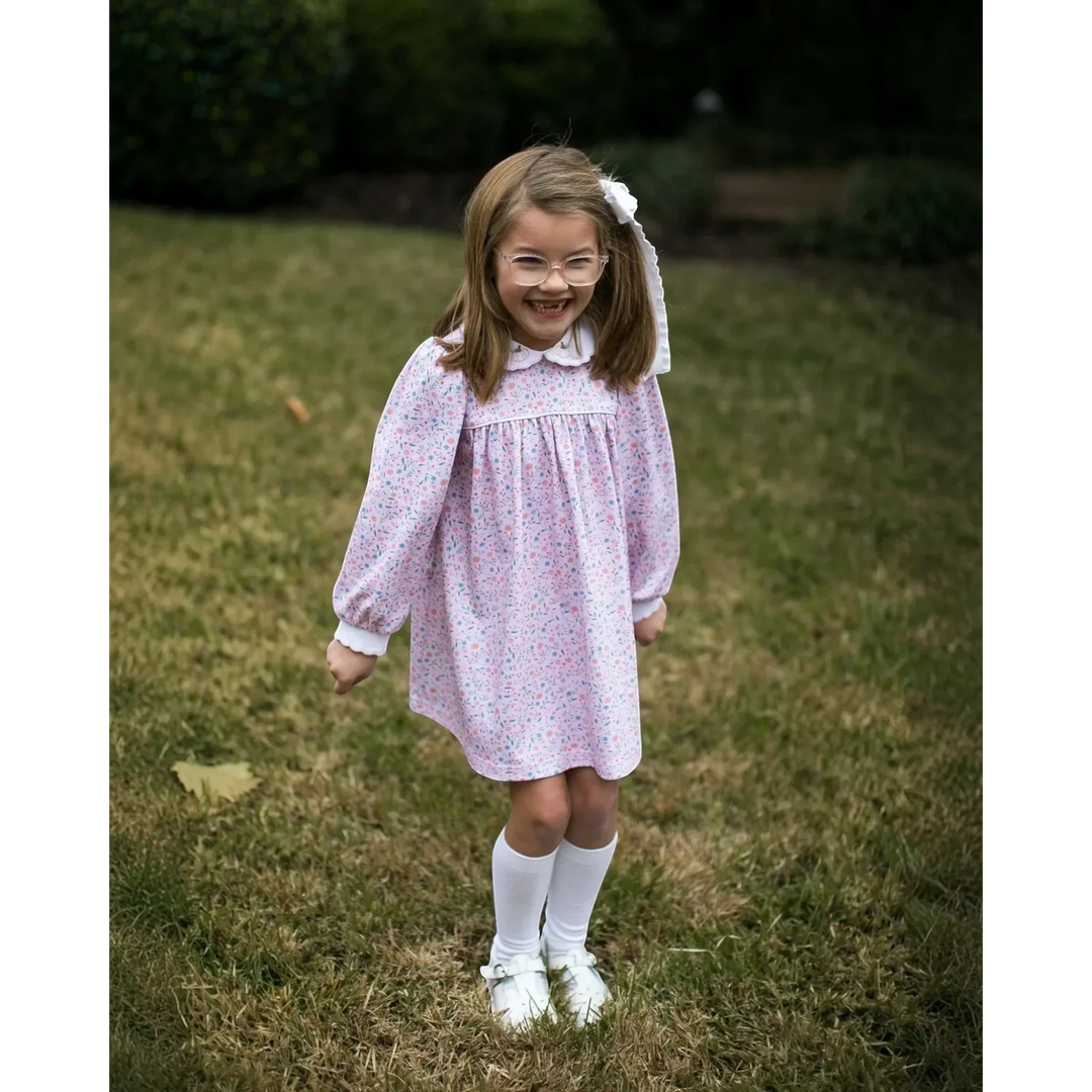 Young girl wearing a That Store long sleeve floral dress with pumpkin embroidery on the collar in a grassy field