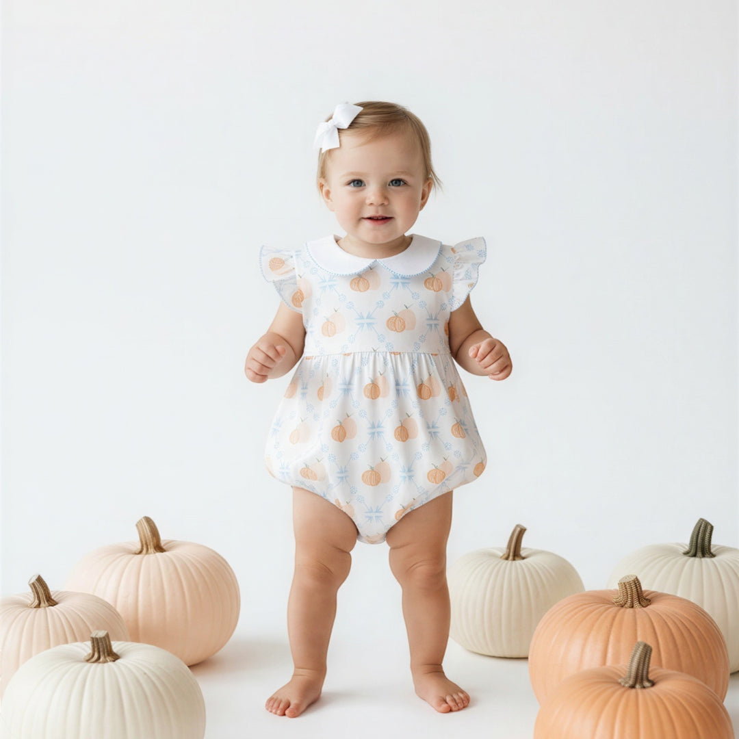 That Store baby girl wearing a white bubble romper with a pumpkin print, Peter Pan collar, and ruffled sleeves.
