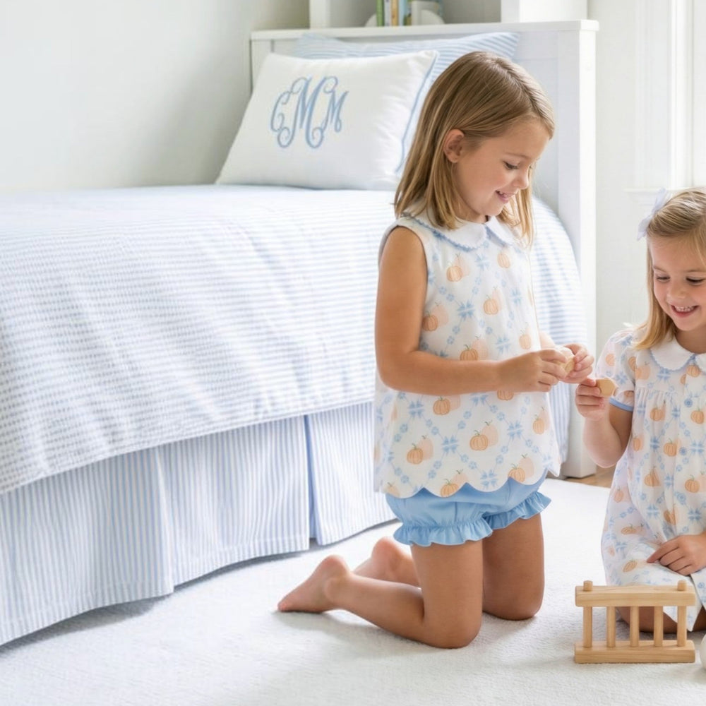Two girls wearing That Store Pumpkin Row Charlotte scalloped pumpkin print bloomer sets in a bright bedroom