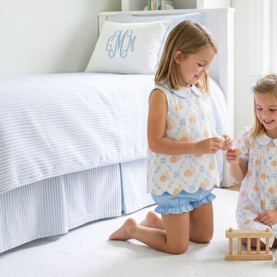 Two girls wearing That Store Pumpkin Row Charlotte scalloped pumpkin print bloomer sets in a bright bedroom