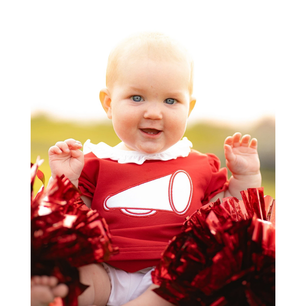 Baby girl wearing a That Store red cotton bloomer set with a white megaphone applique and ruffled collar