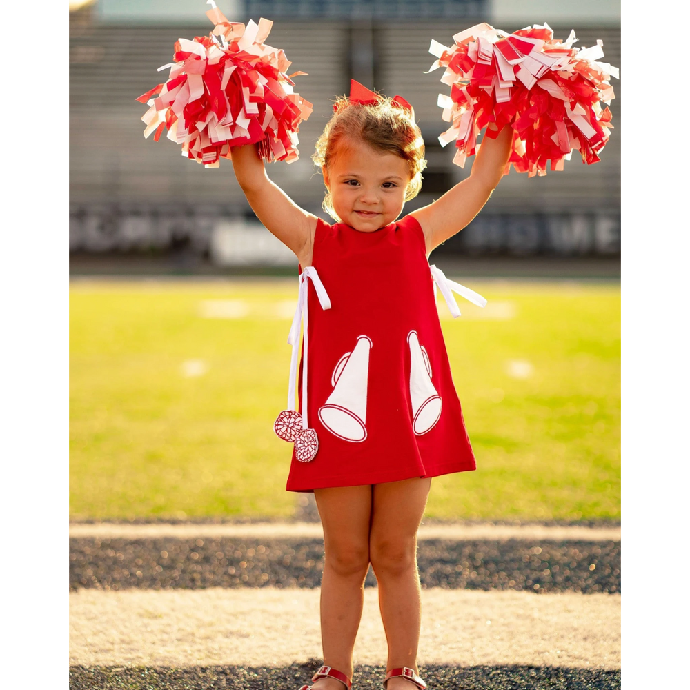 That Store red cotton jumper dress with megaphone appliques and pom-pom ties worn by a girl holding cheer pom-poms
