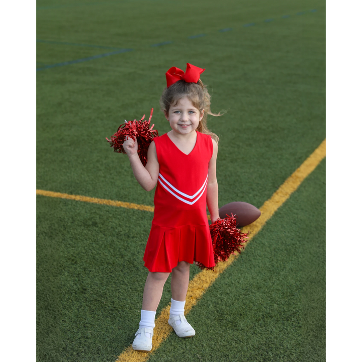 Young girl wearing a That Store red cheer uniform dress with white stripes and holding red pom-poms on a football field