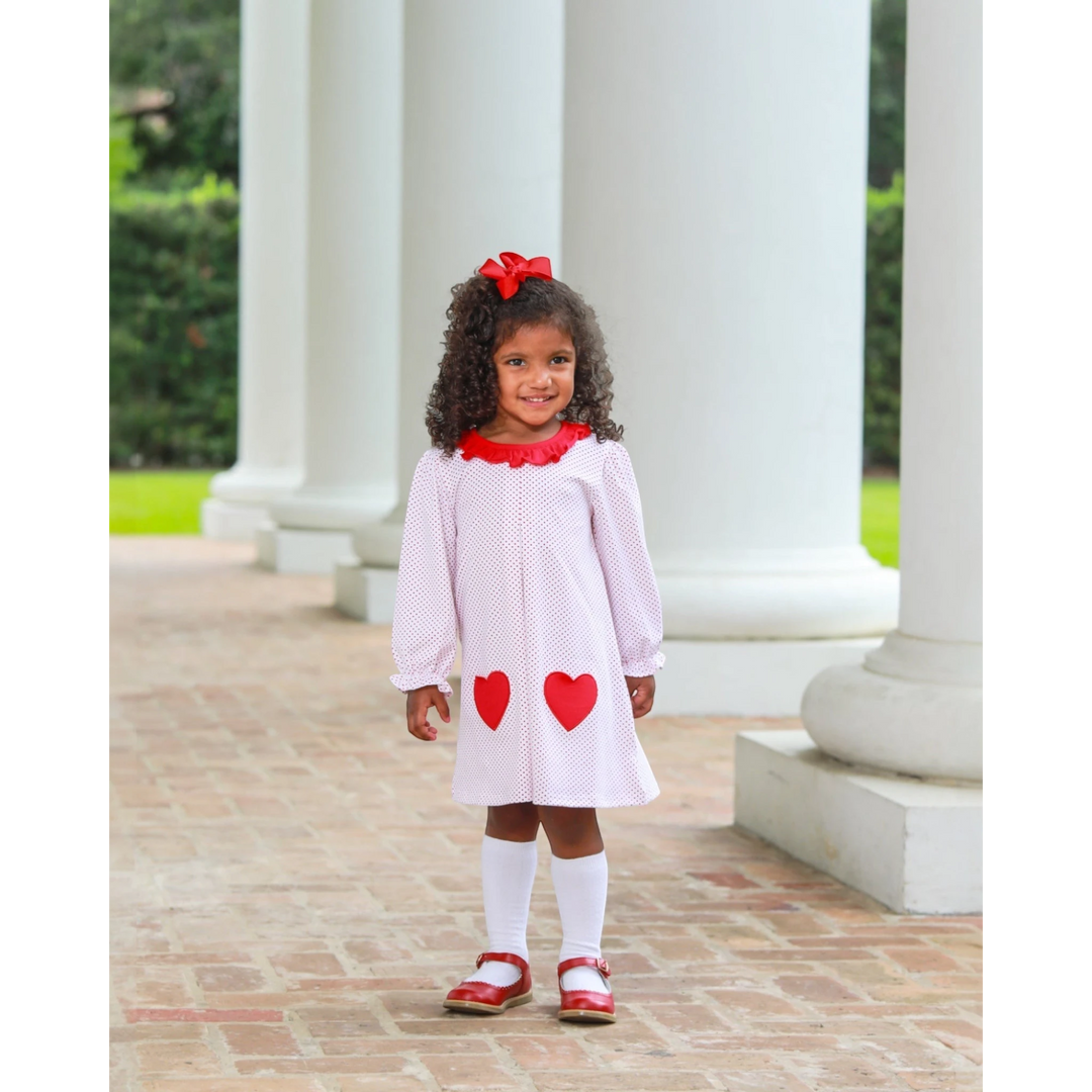 A young girl wearing a That Store red dot heart dress with appliqué hearts and a matching red hair bow