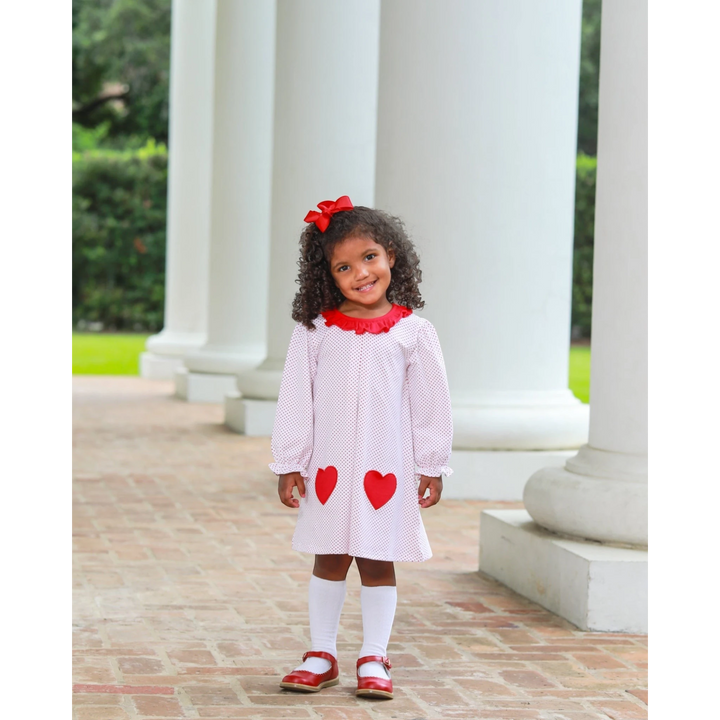 That Store red dot heart dress with ruffled collar worn by a smiling girl with a red hair bow and red shoes
