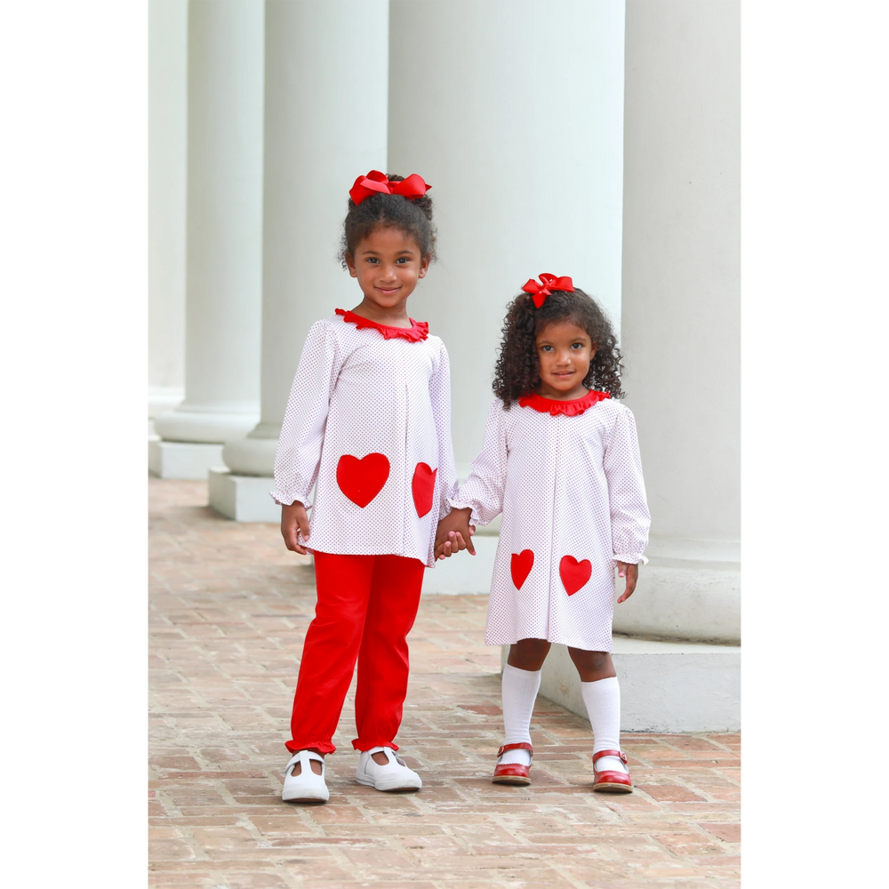 Two girls wearing That Store red dot heart outfits with matching hair bows standing between white pillars.