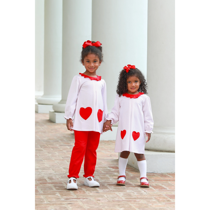 Two girls wearing That Store red dot heart outfits with matching hair bows standing between white pillars.