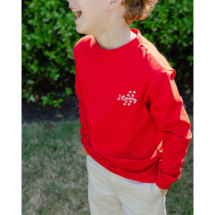That Store red long sleeve cotton tee with J.Bailey logo and paw prints worn by a laughing boy outdoors