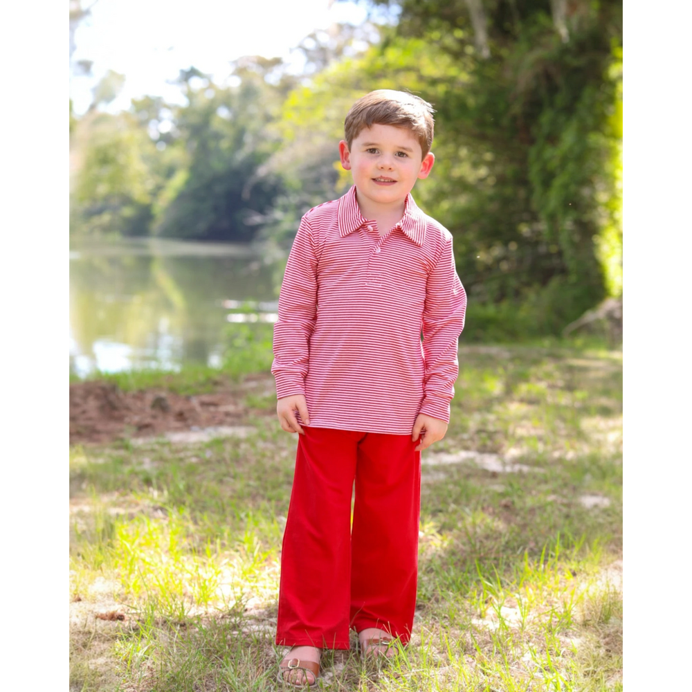 Young boy wearing a That Store Jackson Polo with red and white stripes and red trousers in a park setting.
