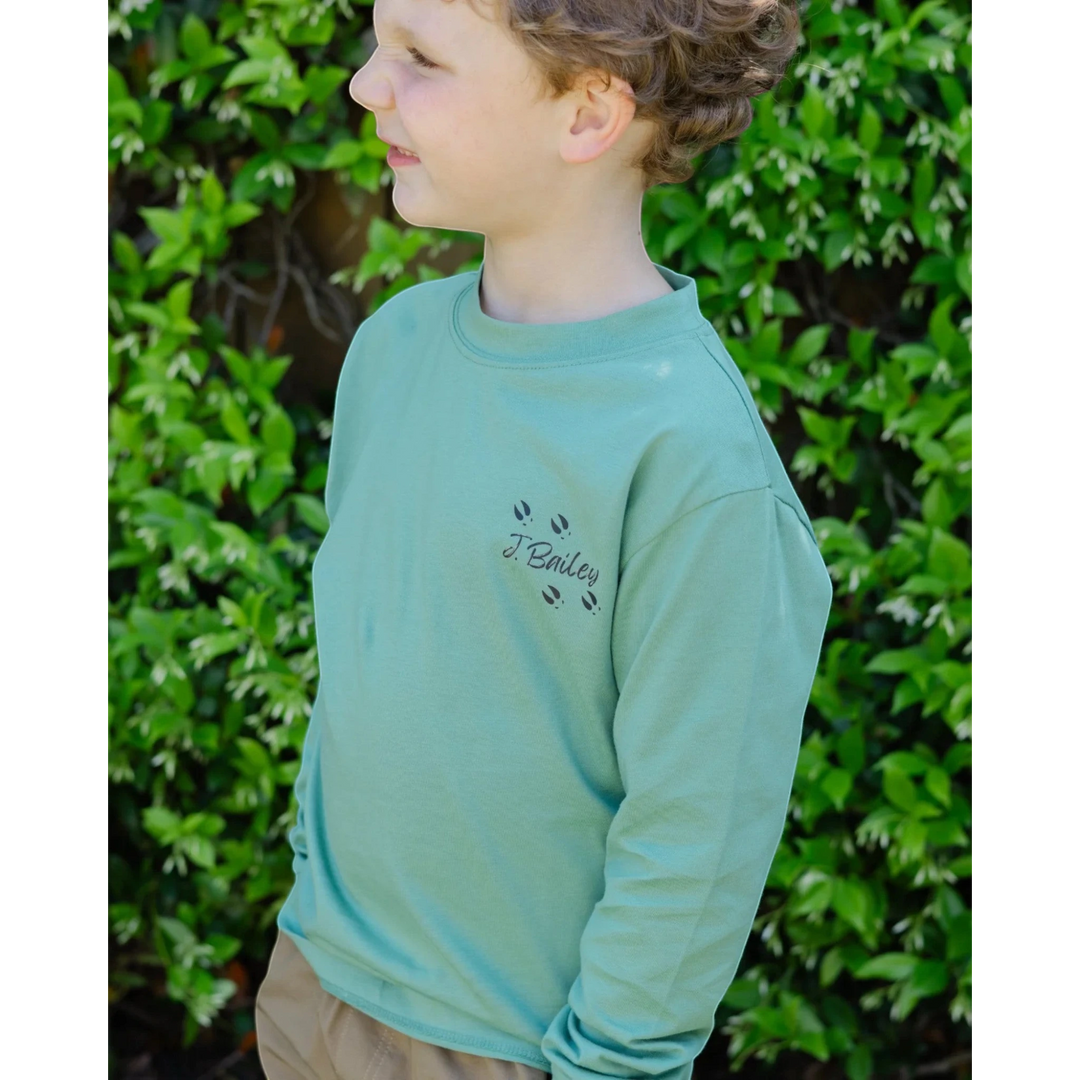 That Store sage green long sleeve cotton tee with J. Bailey logo and deer tracks on a young boy outdoors