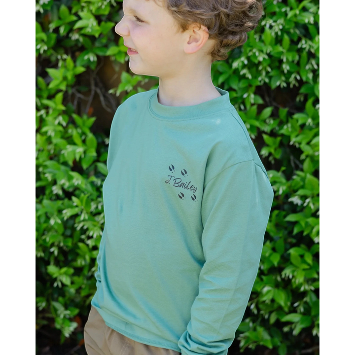 That Store sage green long sleeve cotton tee with J. Bailey logo and deer tracks on a young boy outdoors