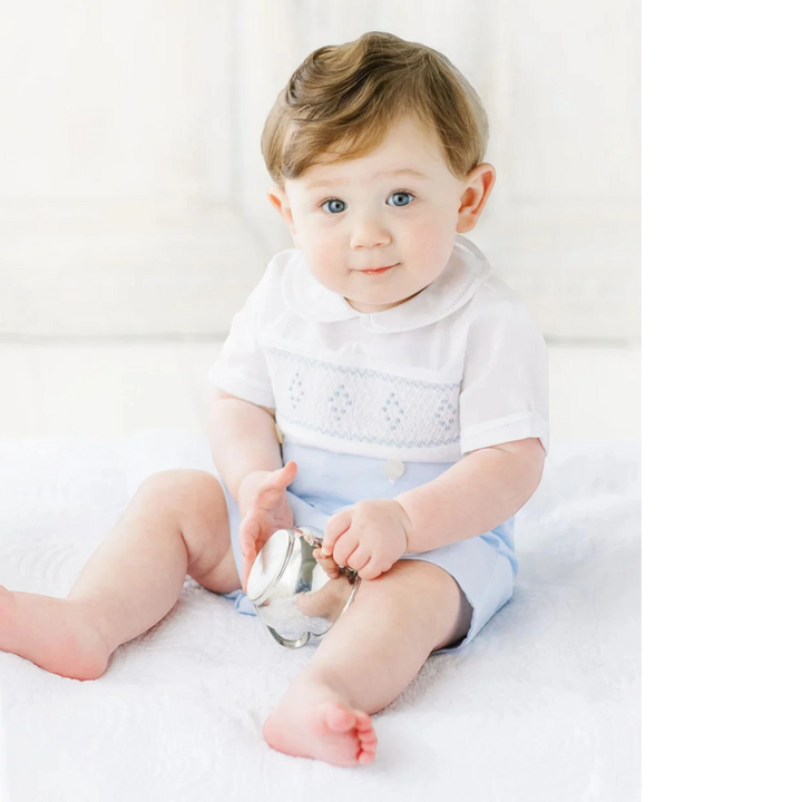 That Store baby boy wearing a white and blue smocked bobby suit with a peter pan collar and hand-made embroidery.