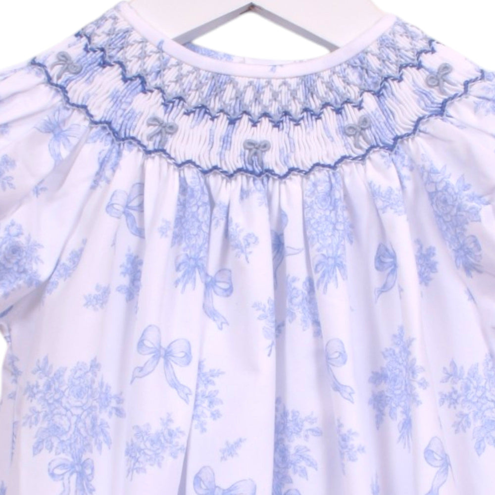 That Store girls bubble in white with blue floral print, featuring intricate smocking and blue bows at the neckline.