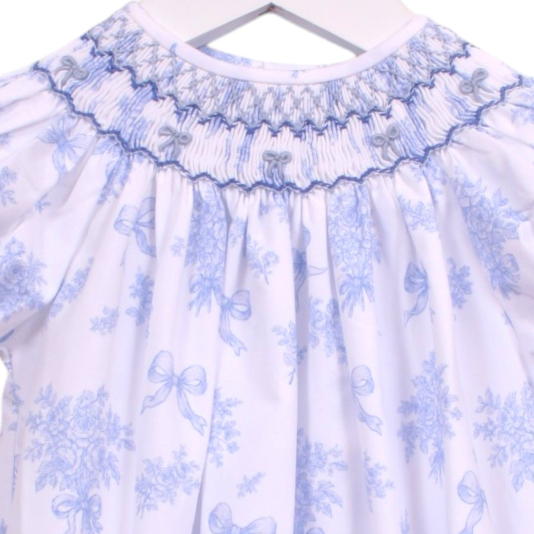 That Store girls bubble in white with blue floral print, featuring intricate smocking and blue bows at the neckline.