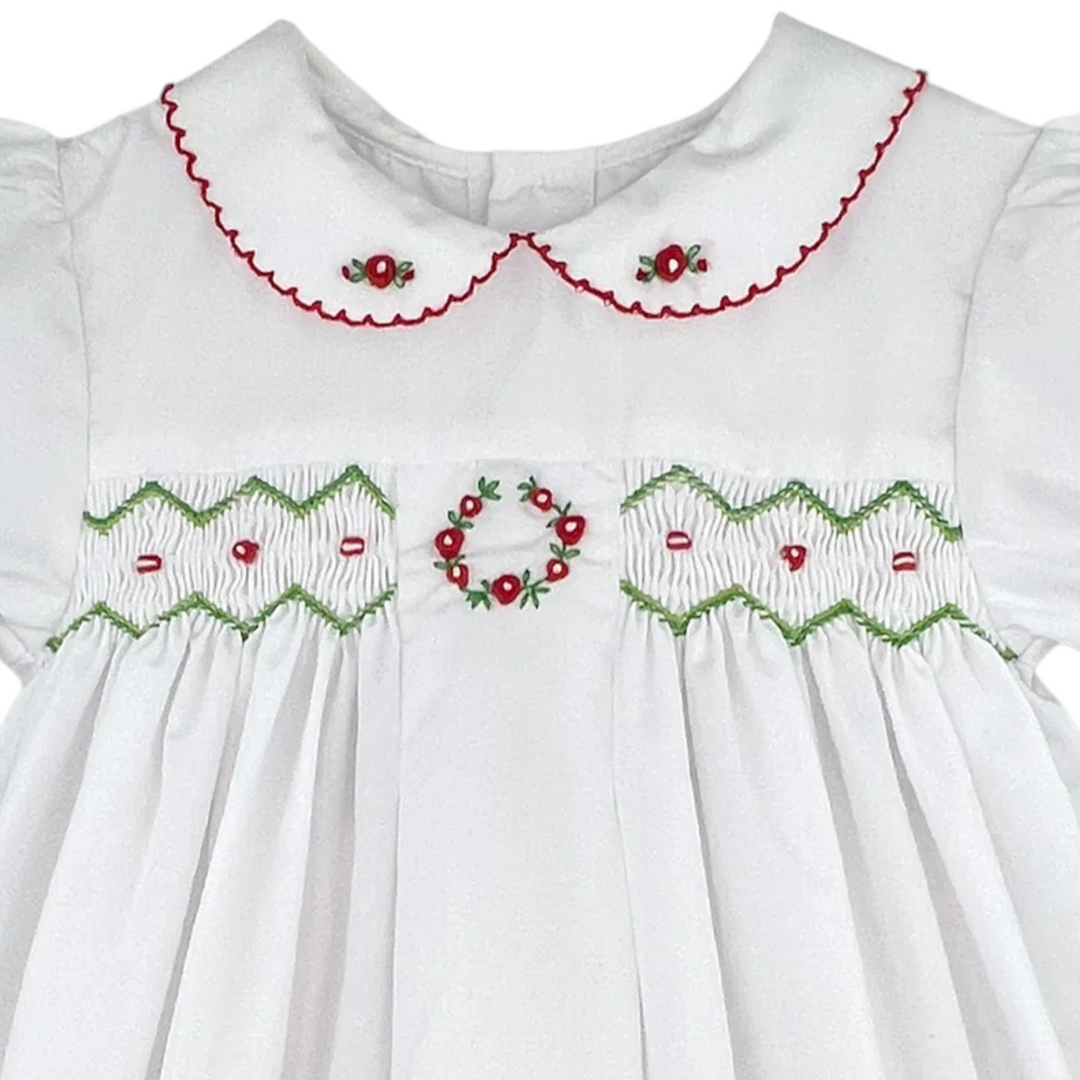 That Store white holiday dress for girls featuring red and green smocking, floral embroidery, and a scalloped collar.