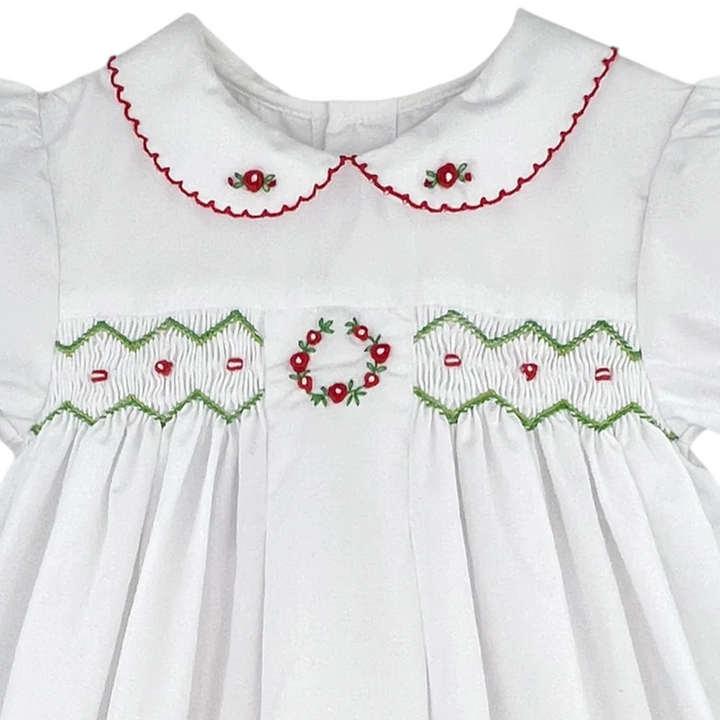That Store white holiday dress for girls featuring red and green smocking, floral embroidery, and a scalloped collar.