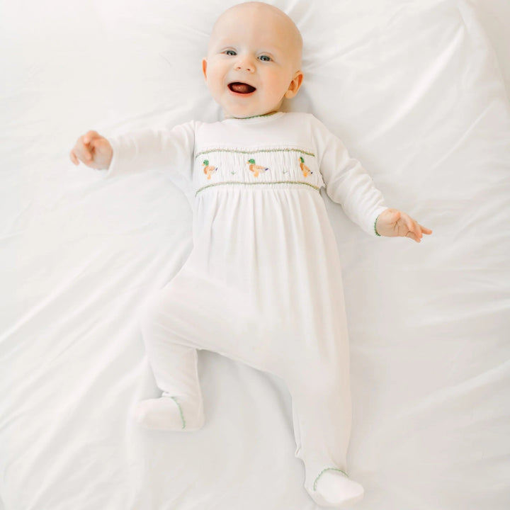 Happy baby wearing a white That Store smocked footie with mallard duck embroidery in soft Peruvian Pima cotton