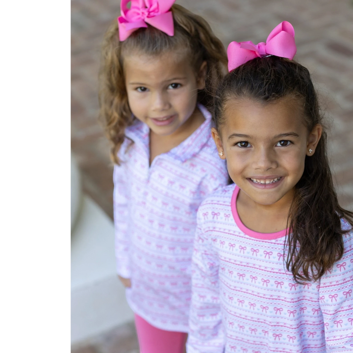 Two young girls wearing That Store Sweetheart French Terry tunic sets with pink bows in their hair