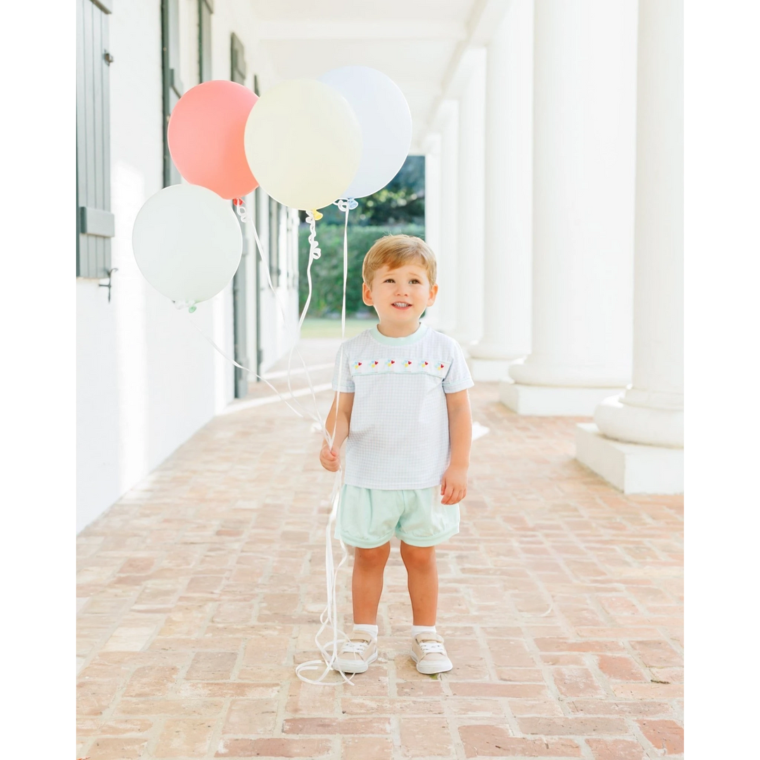 That Store toddler boy wearing a light blue gingham short set with Mickey balloon embroidery holding colorful balloons