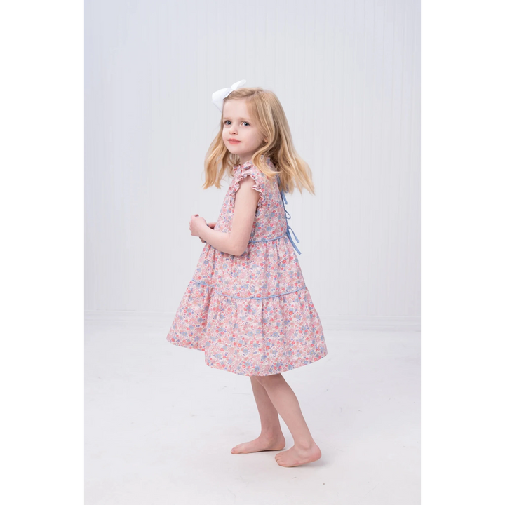 That Store Valeria pink and blue floral dress with ruffle sleeves and a white hair bow worn by a young girl