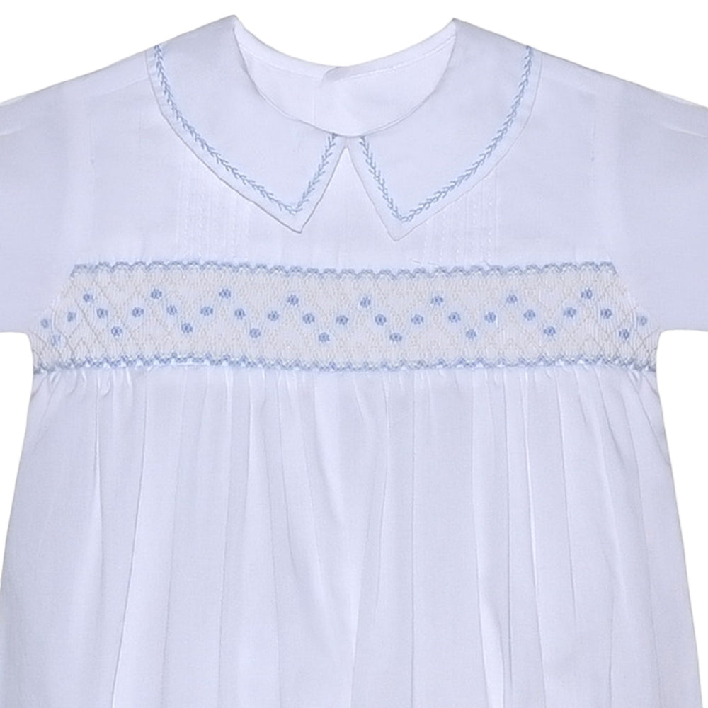 That Store white baby romper with blue geometric smocking, peter pan collar, and delicate embroidery details.